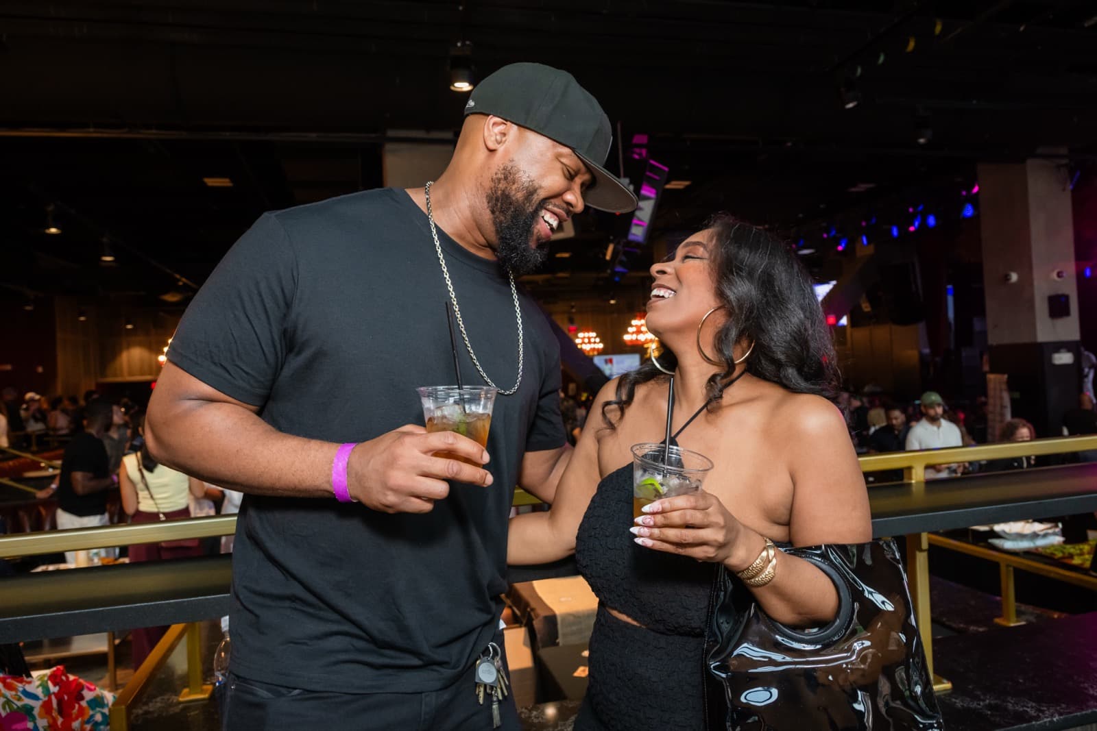 Man and woman laughing together, each holding a drink, at a nightlife event.