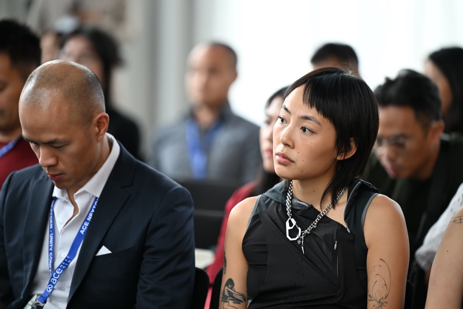 Man and woman seated in an audience, listening attentively, other attendees blurred around them.