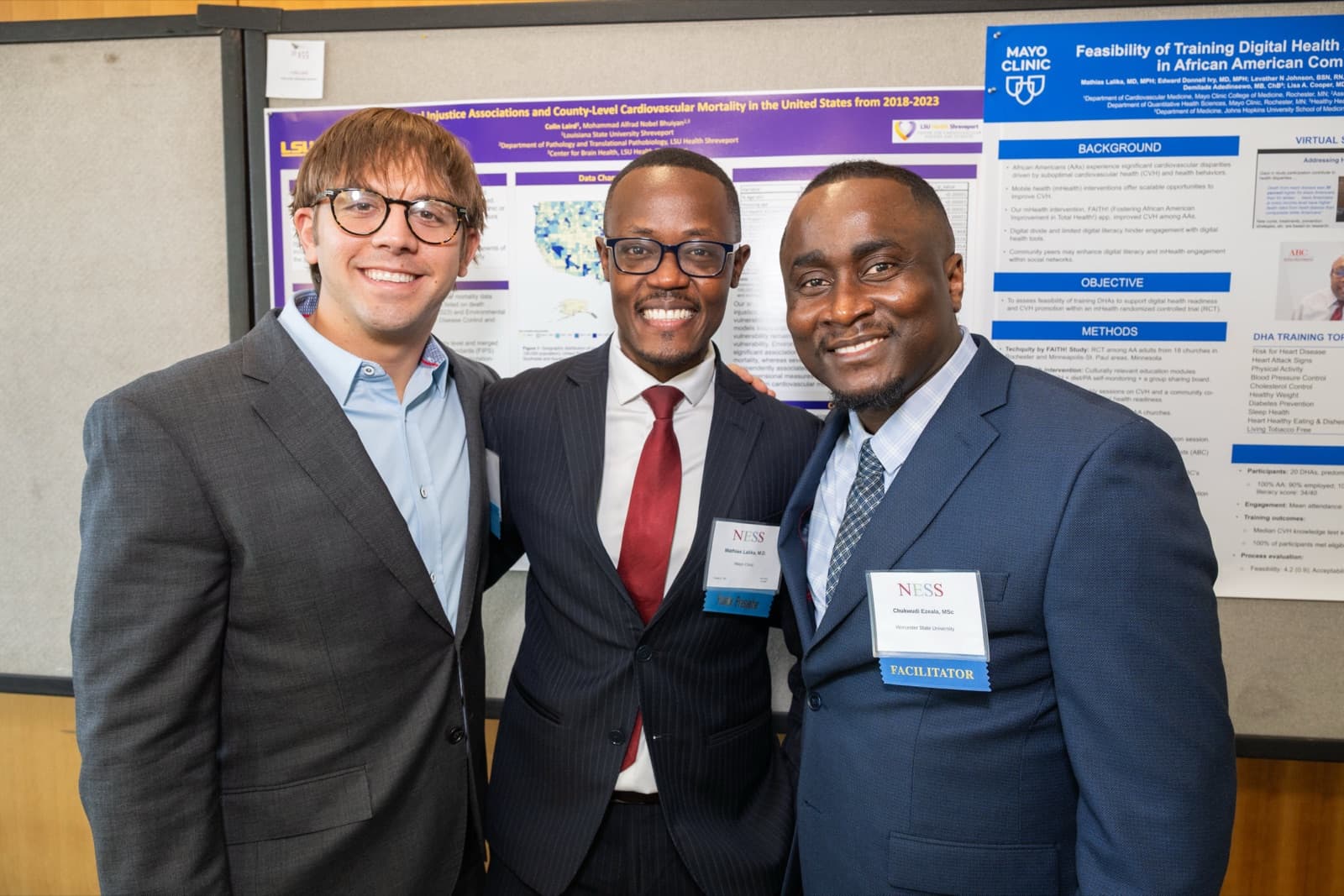 Three men posing together smiling in front of a research poster, all wearing name badges and suits.