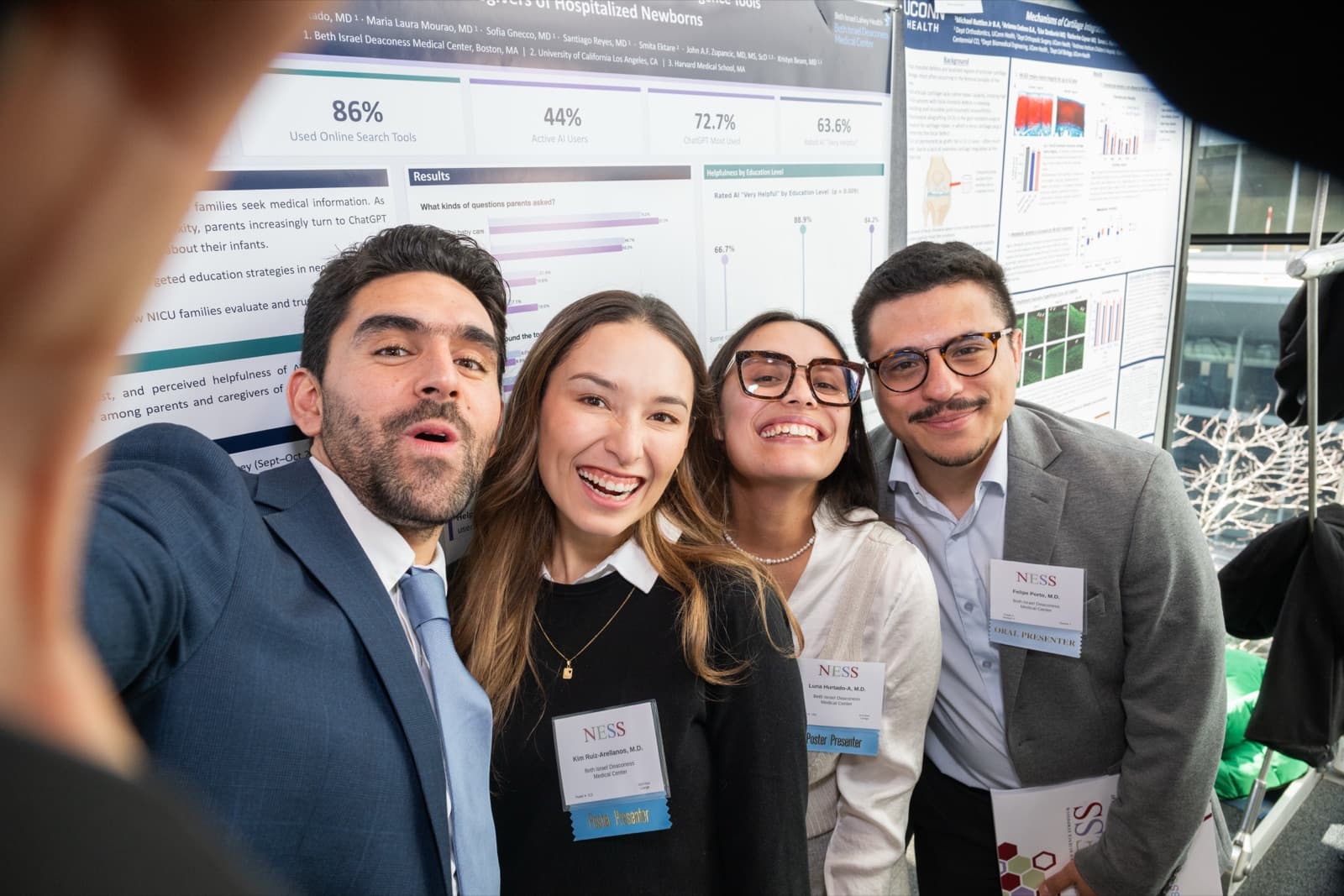 Four people taking a selfie together in front of research posters, grinning.
