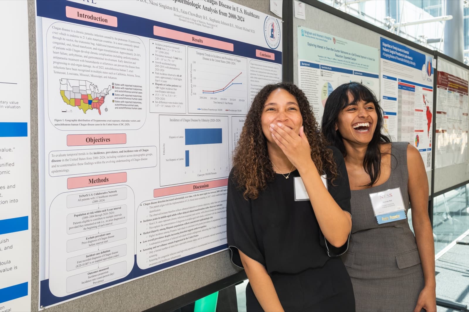 Two women grinning together in a selfie, research posters filled with data behind them.