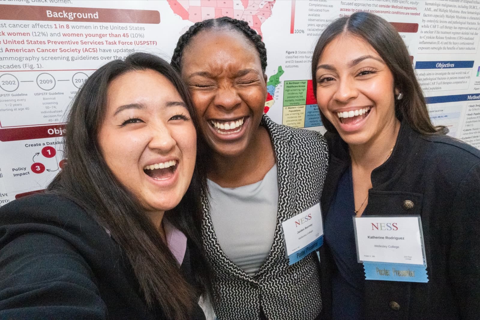 Three women taking a selfie together, one covering her mouth laughing, a research poster behind them.