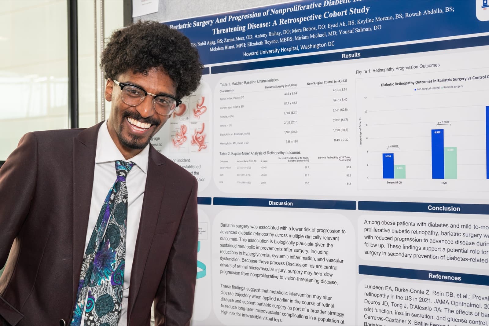 Man with curly hair and glasses smiling broadly in front of a research poster with data tables and charts.