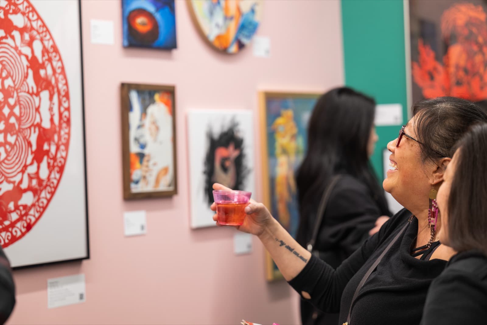 Visitor smiling and raising a drink toward framed paintings, including a red paper-cut circular design.