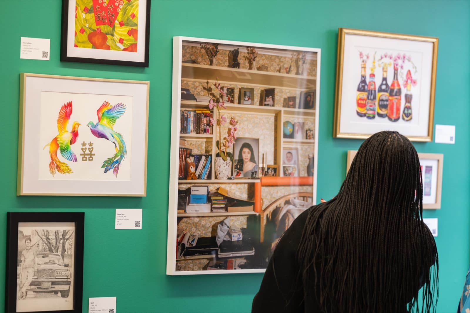 Woman viewing Lunar New Year–themed artwork, including a pair of rainbow phoenixes and a photo collage of a decorated bookshelf.