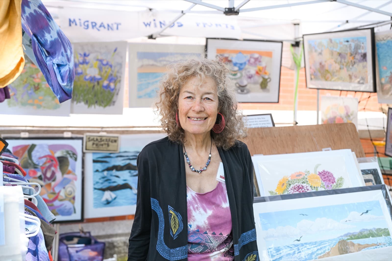 Textile and print artist smiling under a printmaker's banner, hand-dyed scarves and watercolor prints on display.