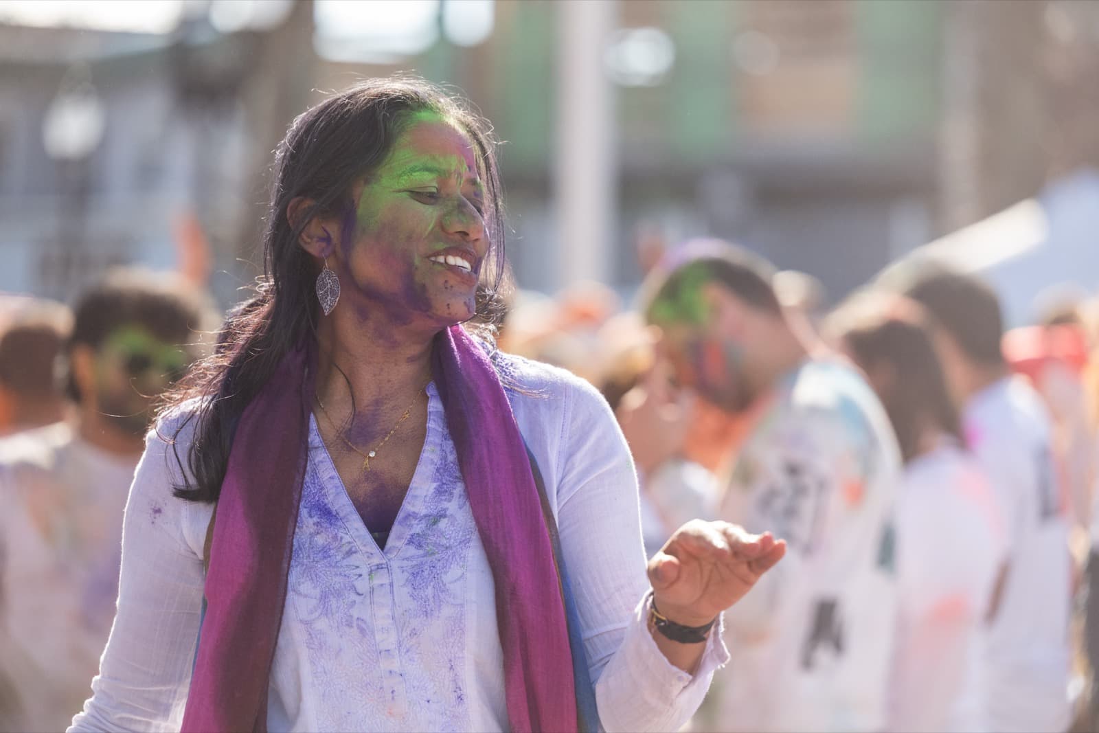 Woman with green and purple powder on her face and a magenta scarf, laughing mid-conversation.