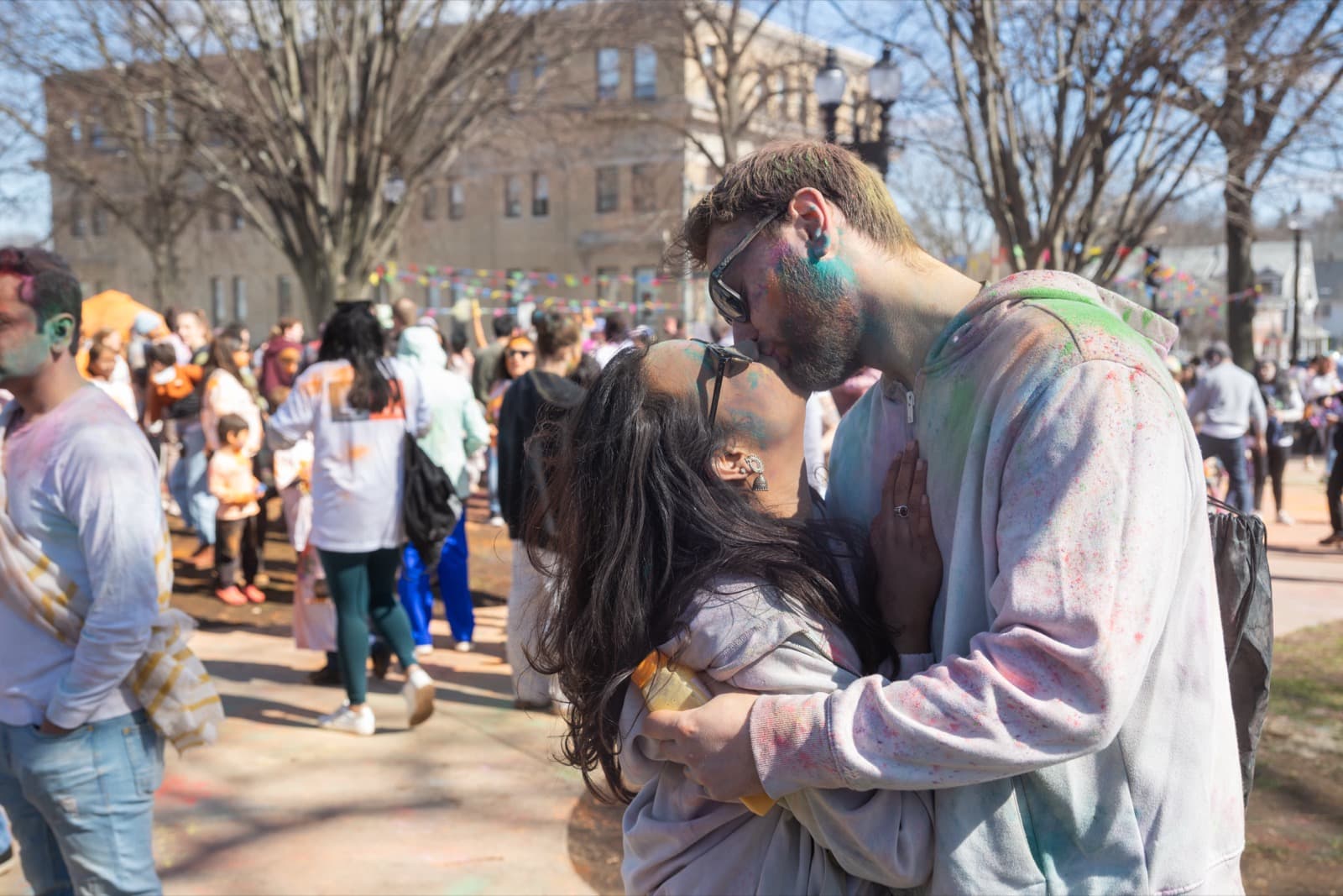 Two people kissing, covered in colored powder, arms wrapped tightly around each other, string pennants strung overhead.