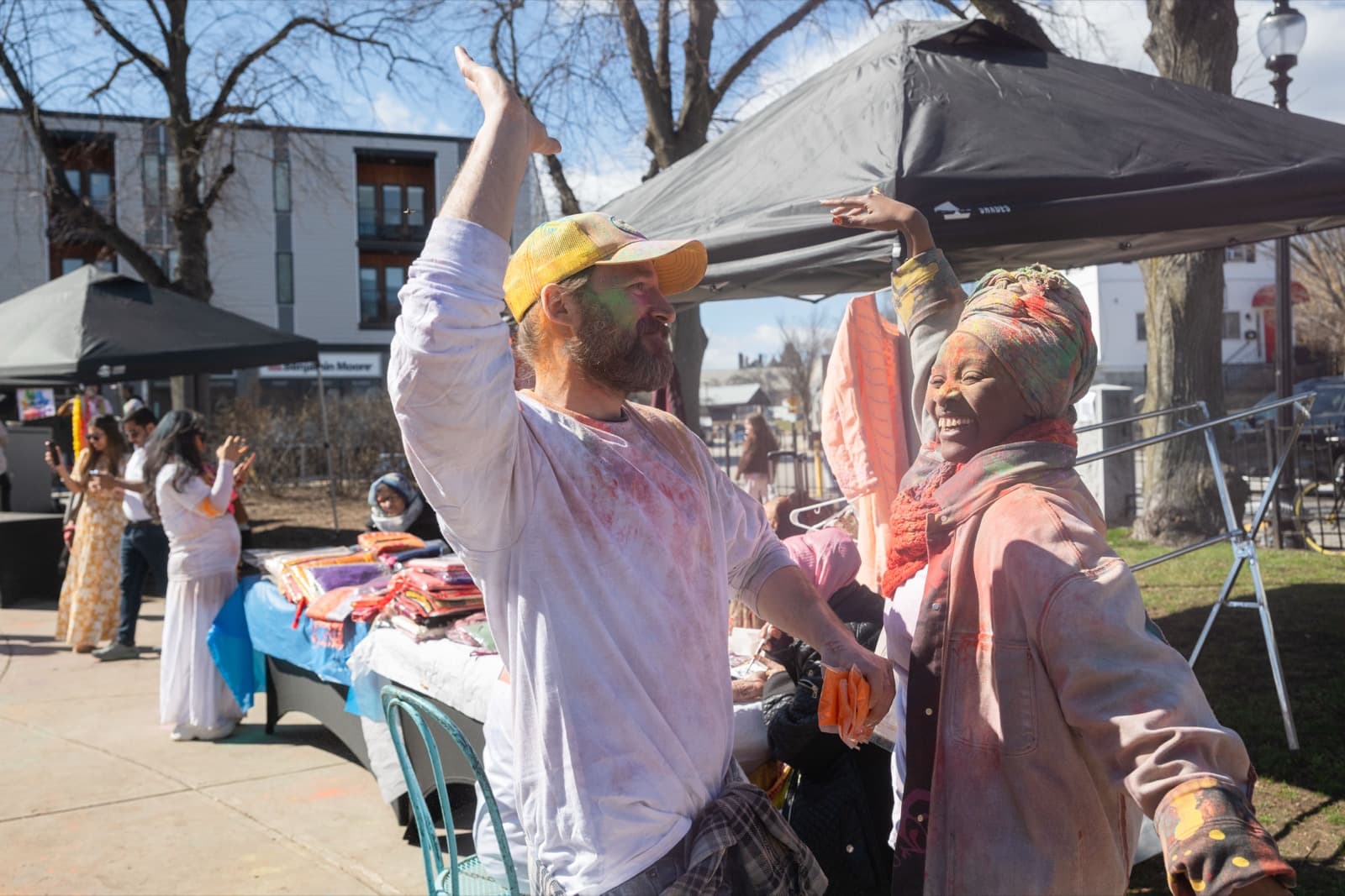 Two people grinning together at a fabric vendor's tent, orange powder covering their shirt and headwrap.