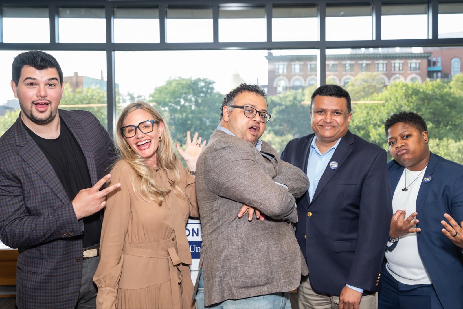 Five people posing playfully, one with arms crossed and a surprised expression, others making peace signs.