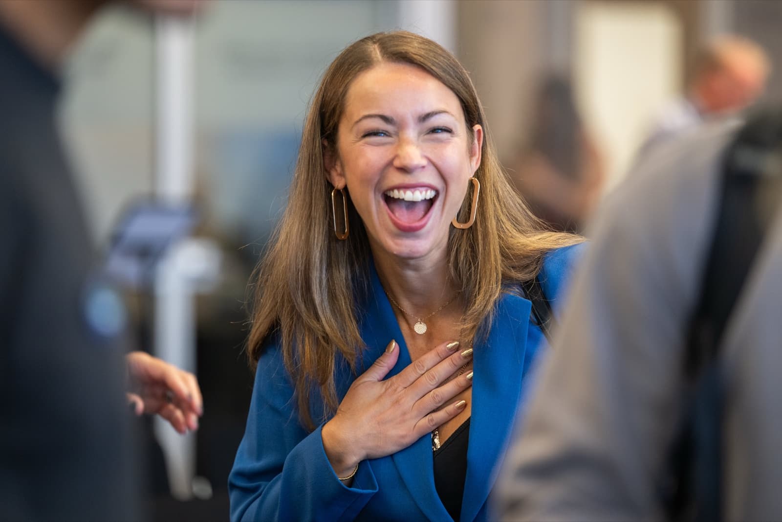 Woman laughing joyfully with a hand on her chest, other attendees blurred around her.