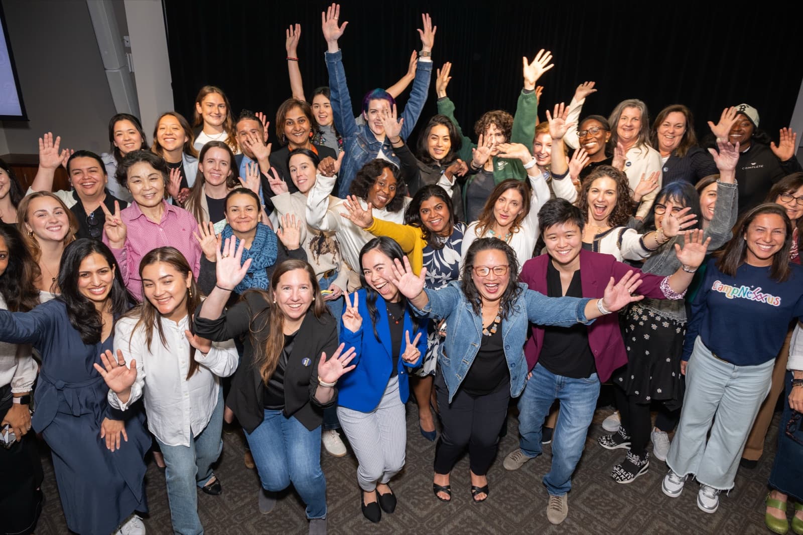 Large group of people cheering together with hands raised high in a conference room.
