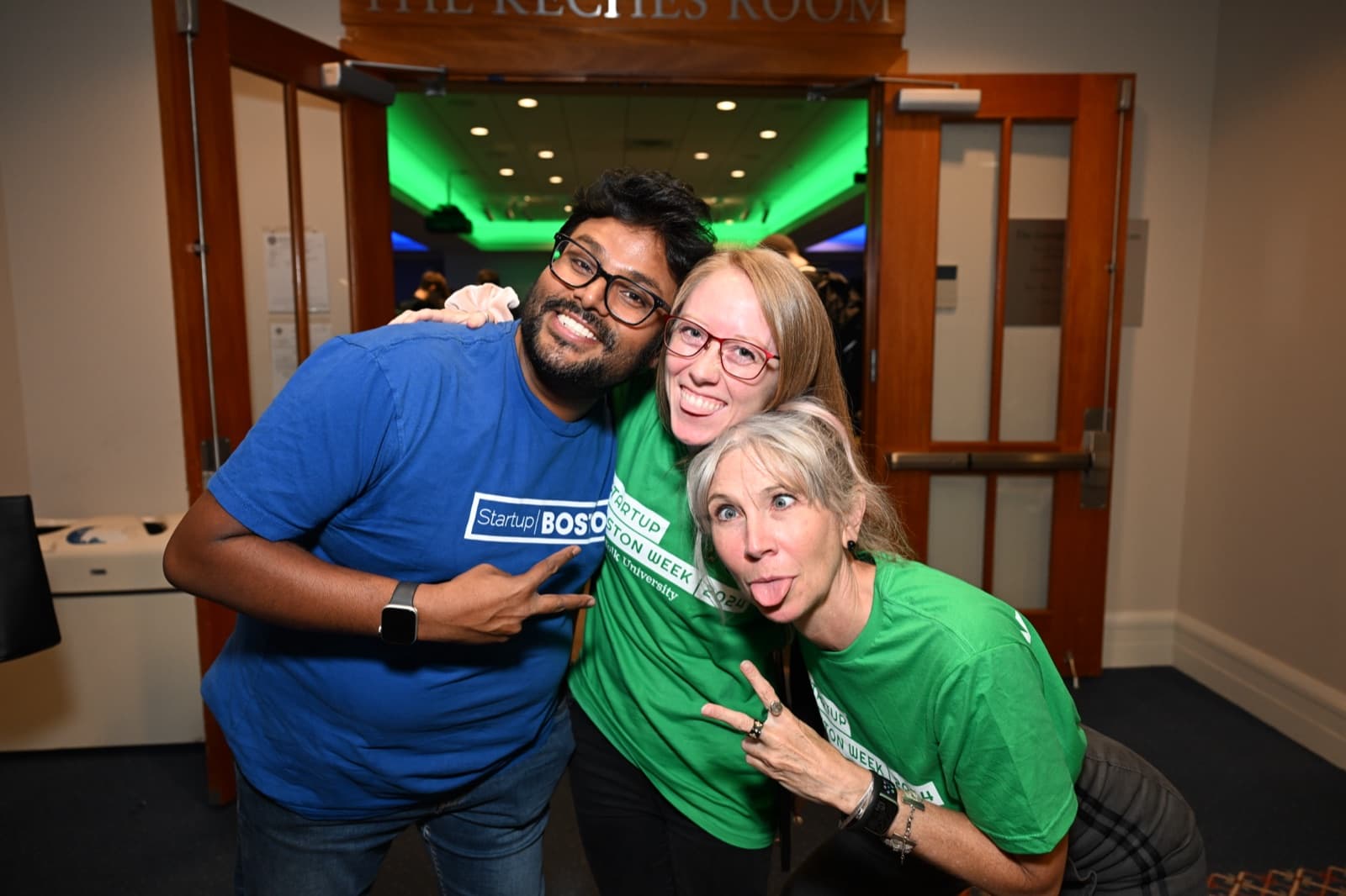 Three people posing playfully, one making a peace sign, one sticking out her tongue, in a doorway.