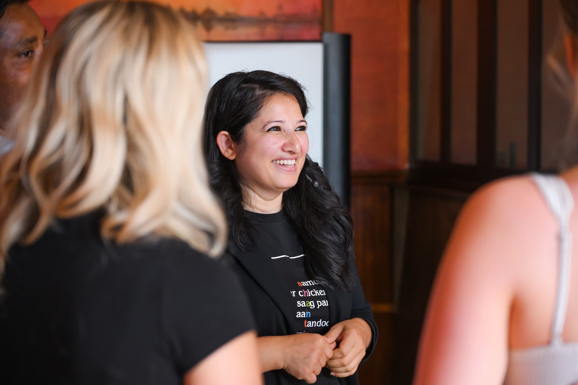 Woman in a graphic t-shirt smiling and talking with others at an indoor gathering.