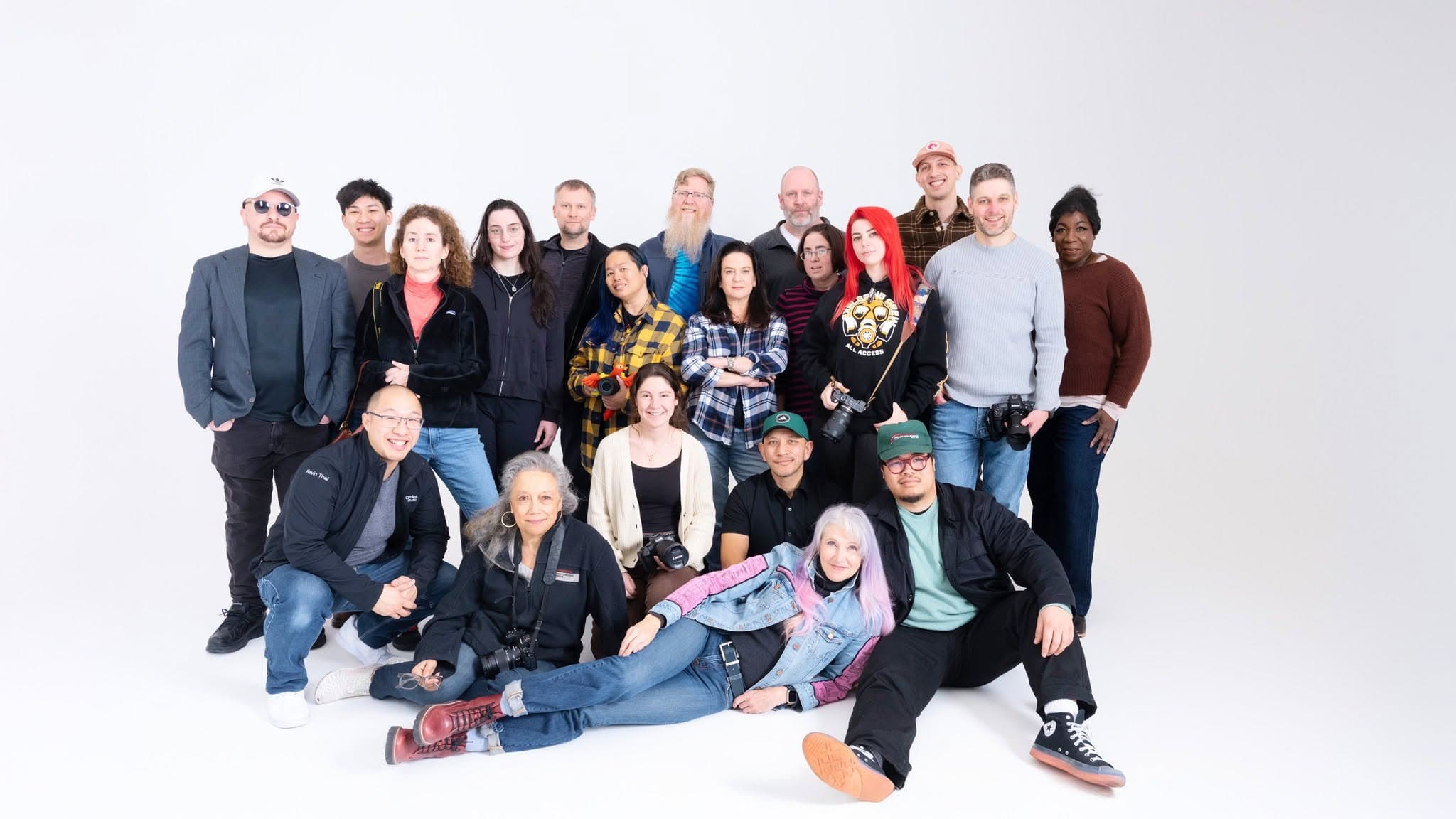 Large group posing together for a photo against a plain white studio background, some holding cameras.