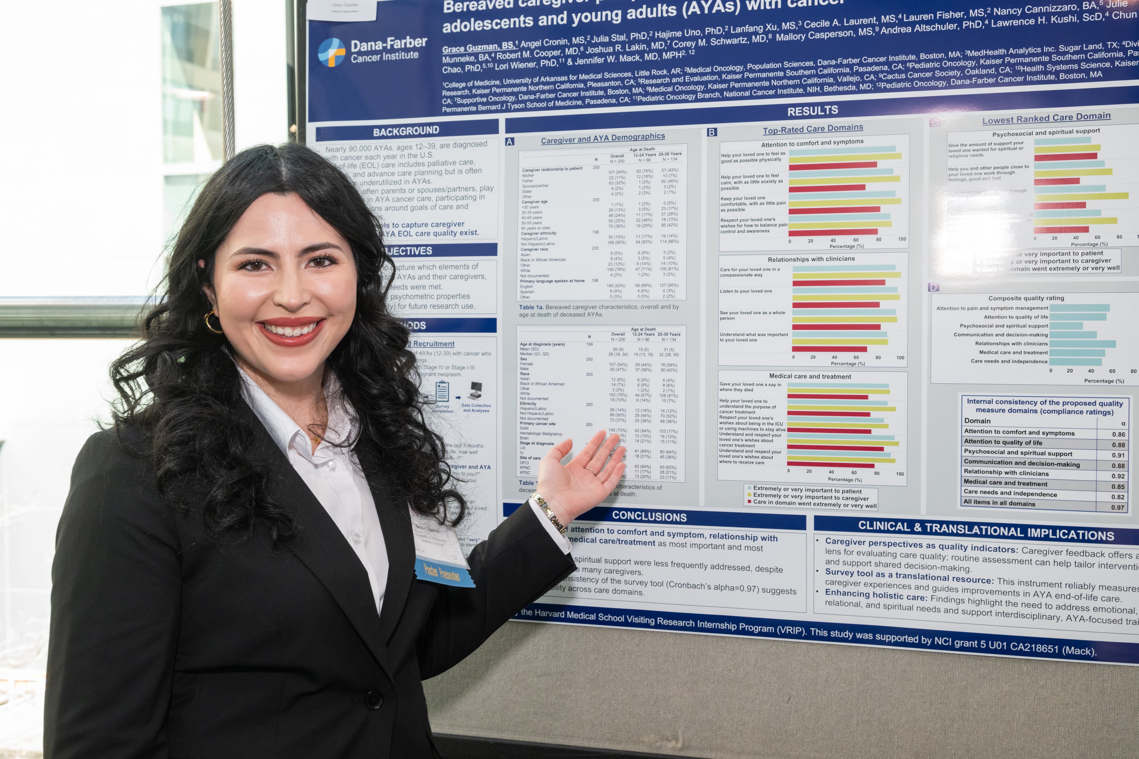 Woman in a blazer smiling and gesturing while presenting at a research poster session.