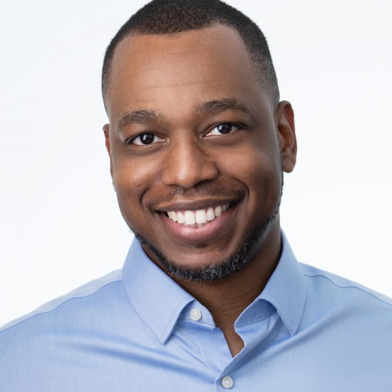 Man with a low fade and light beard smiling in a close studio headshot crop.