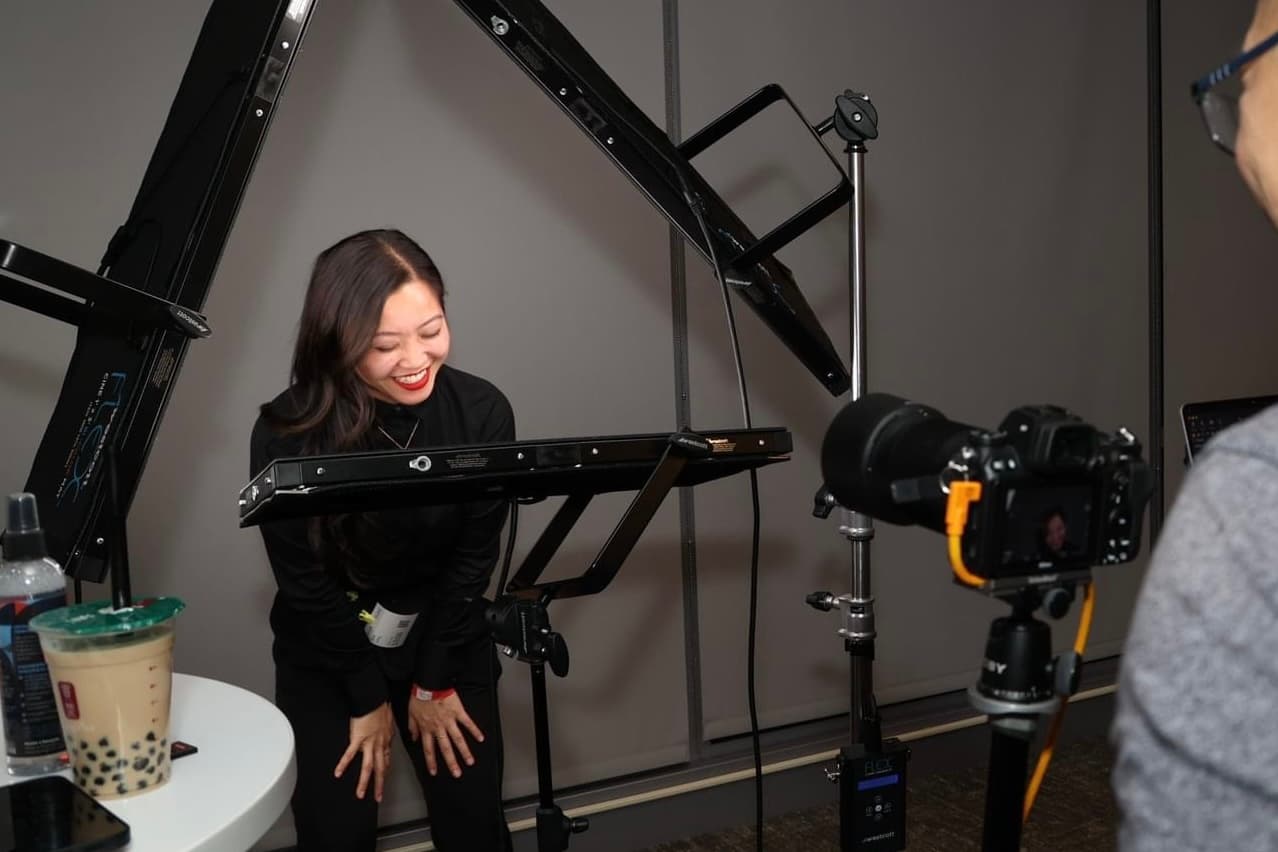 Photographer laughing while adjusting a studio light above a camera on a tripod, mid-session.