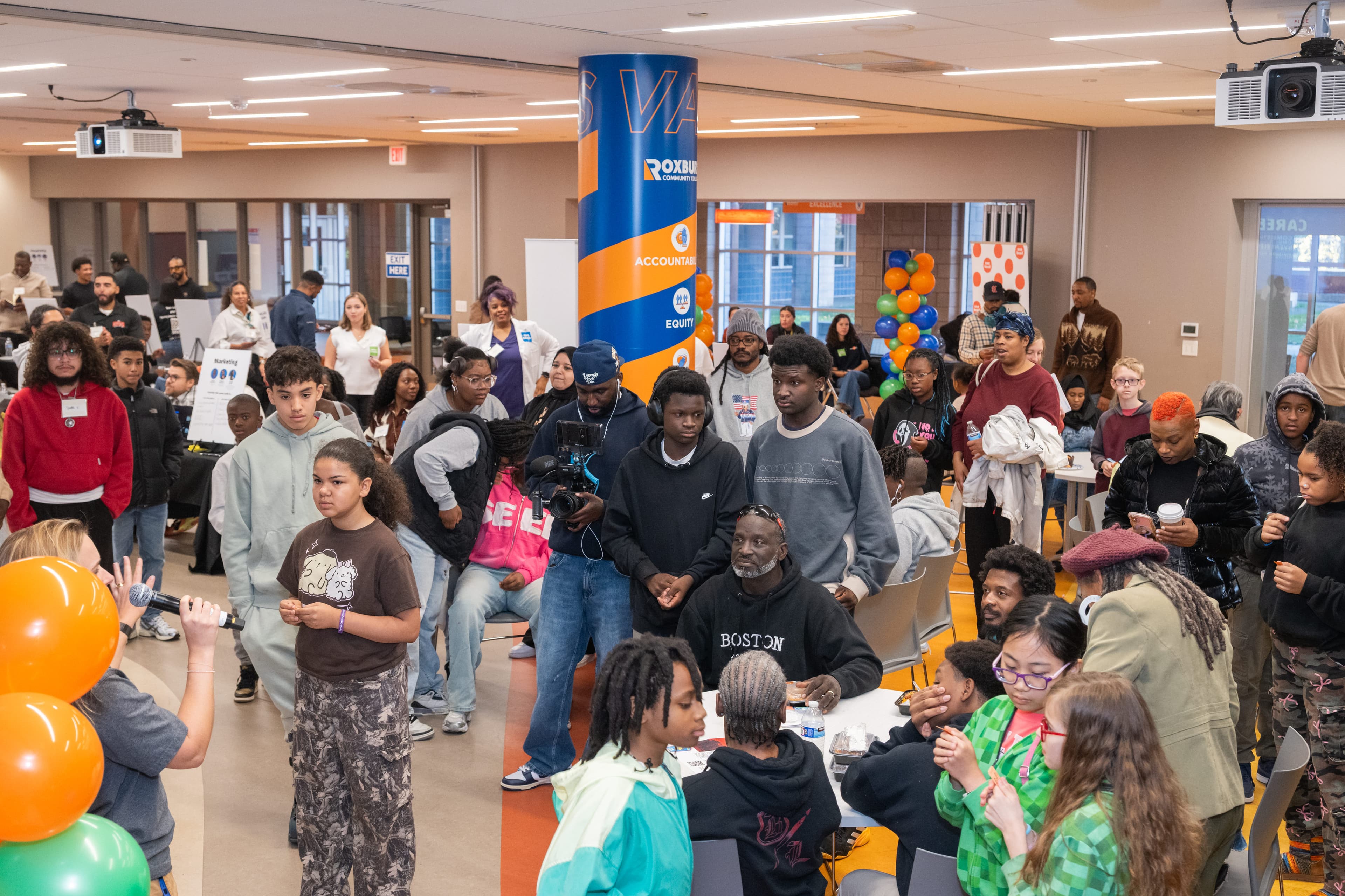 Wide view of a crowded event space with teens and adults, colorful balloon clusters, career expo tables and booths throughout.