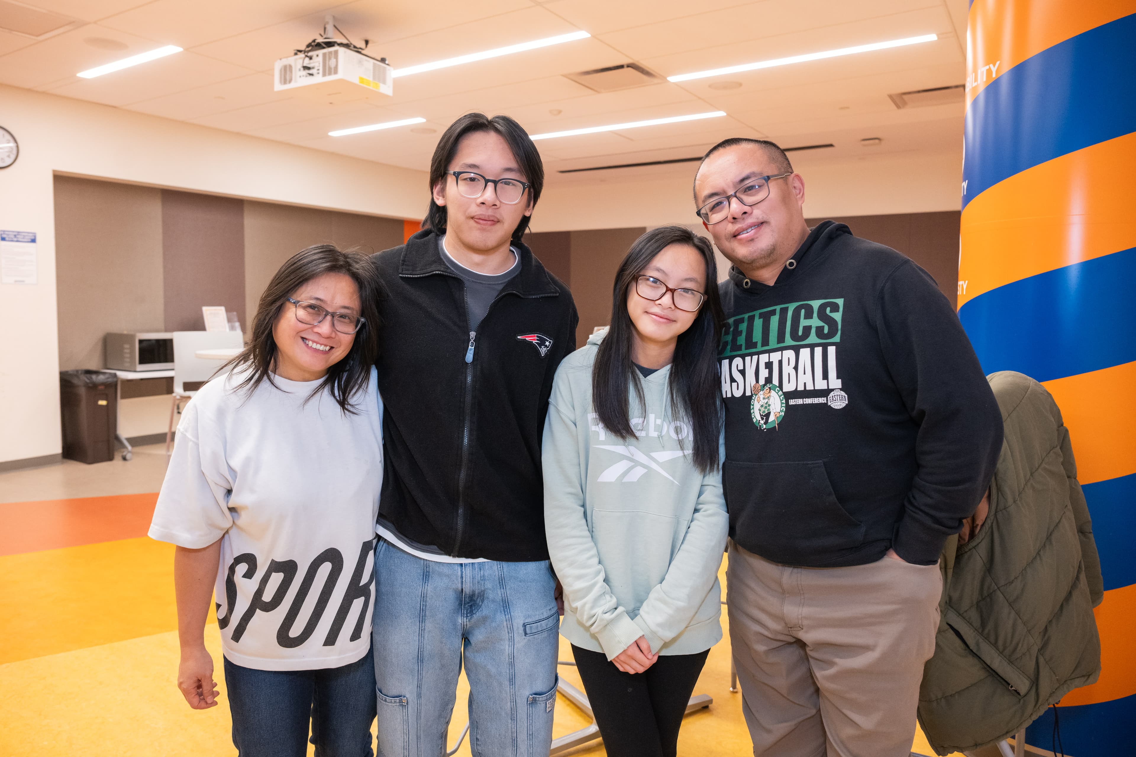 Family of four posing together smiling, wearing branded sports-team clothing, a pillar banner nearby.