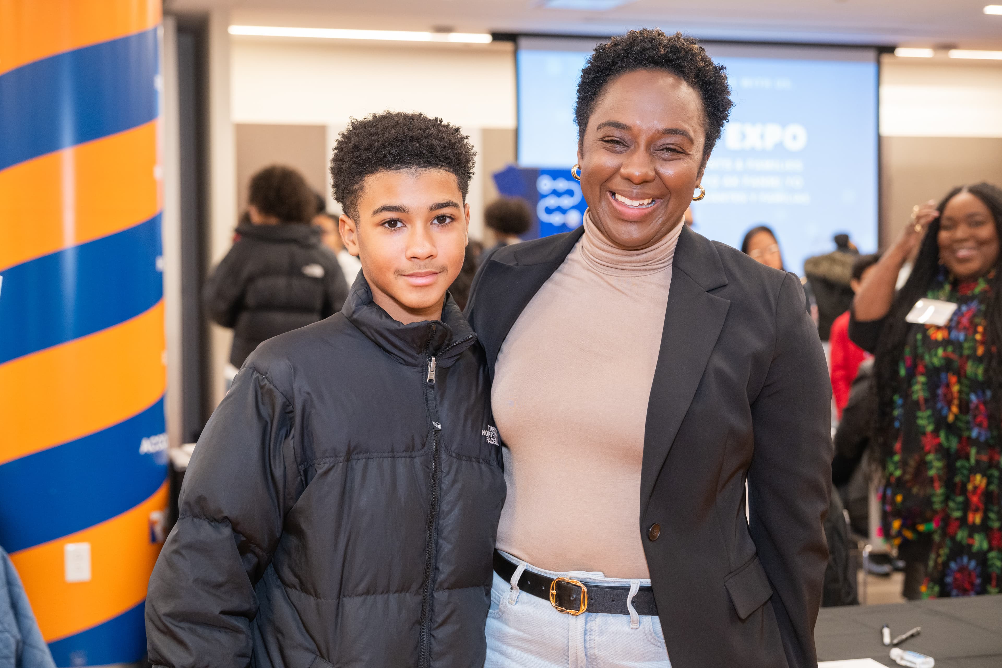 Woman embracing a teenage boy warmly, both smiling, a presentation screen partially visible behind them.