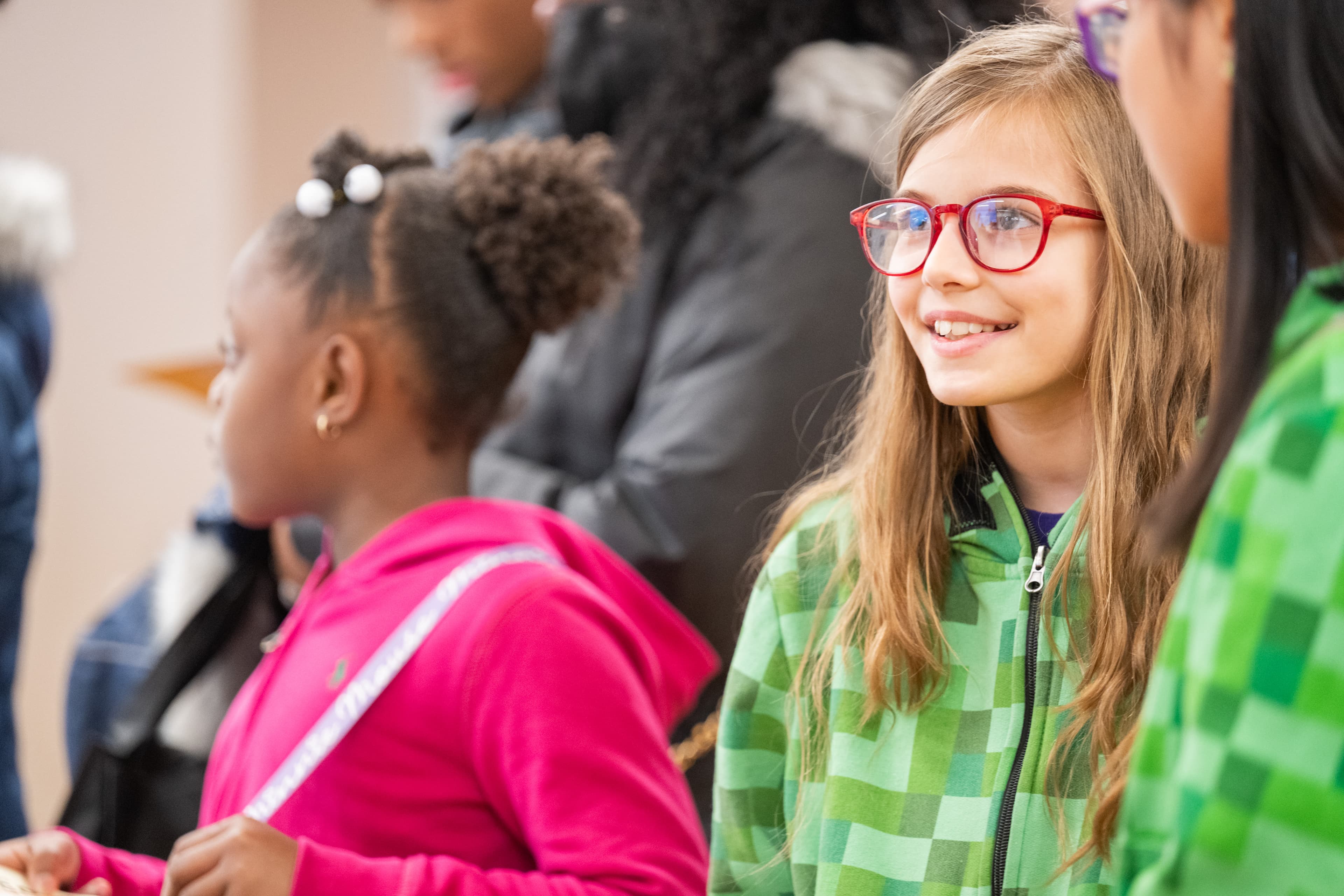 Young girl with glasses smiling and talking, other girls partially visible beside her.