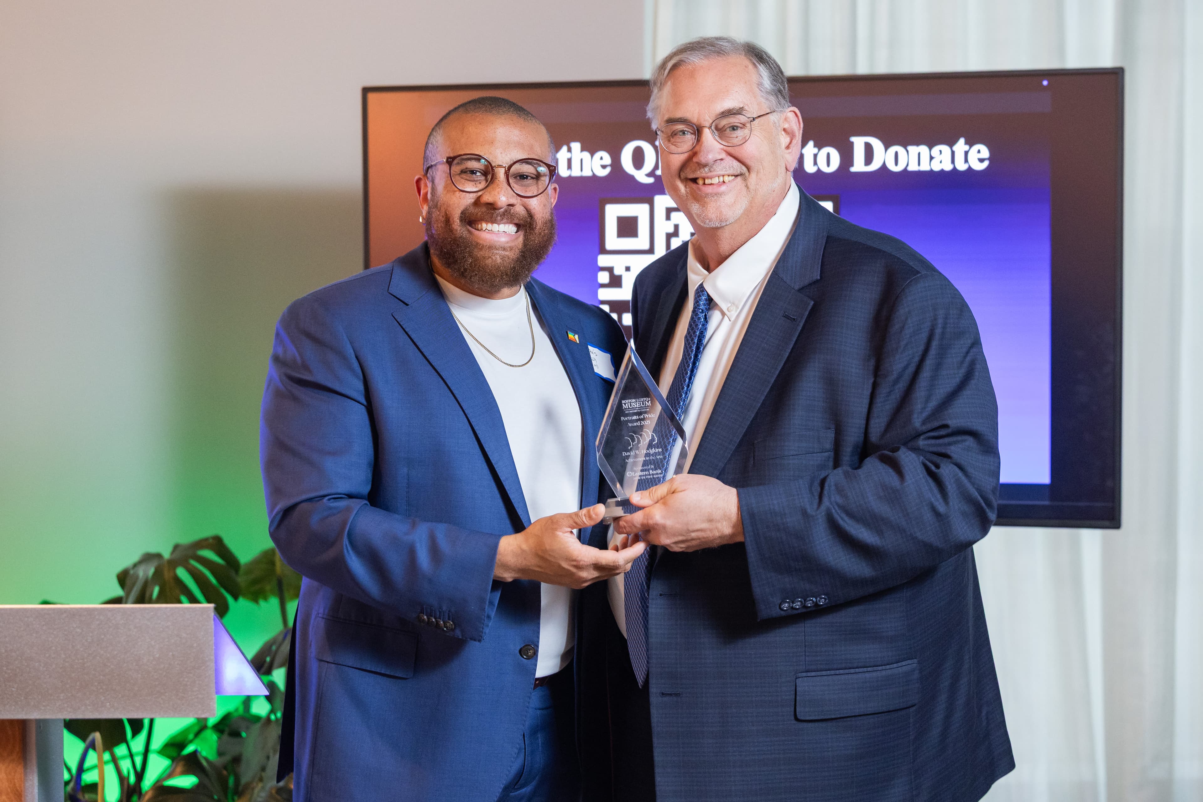 Two men holding a glass award together, smiling, a presentation screen behind them.