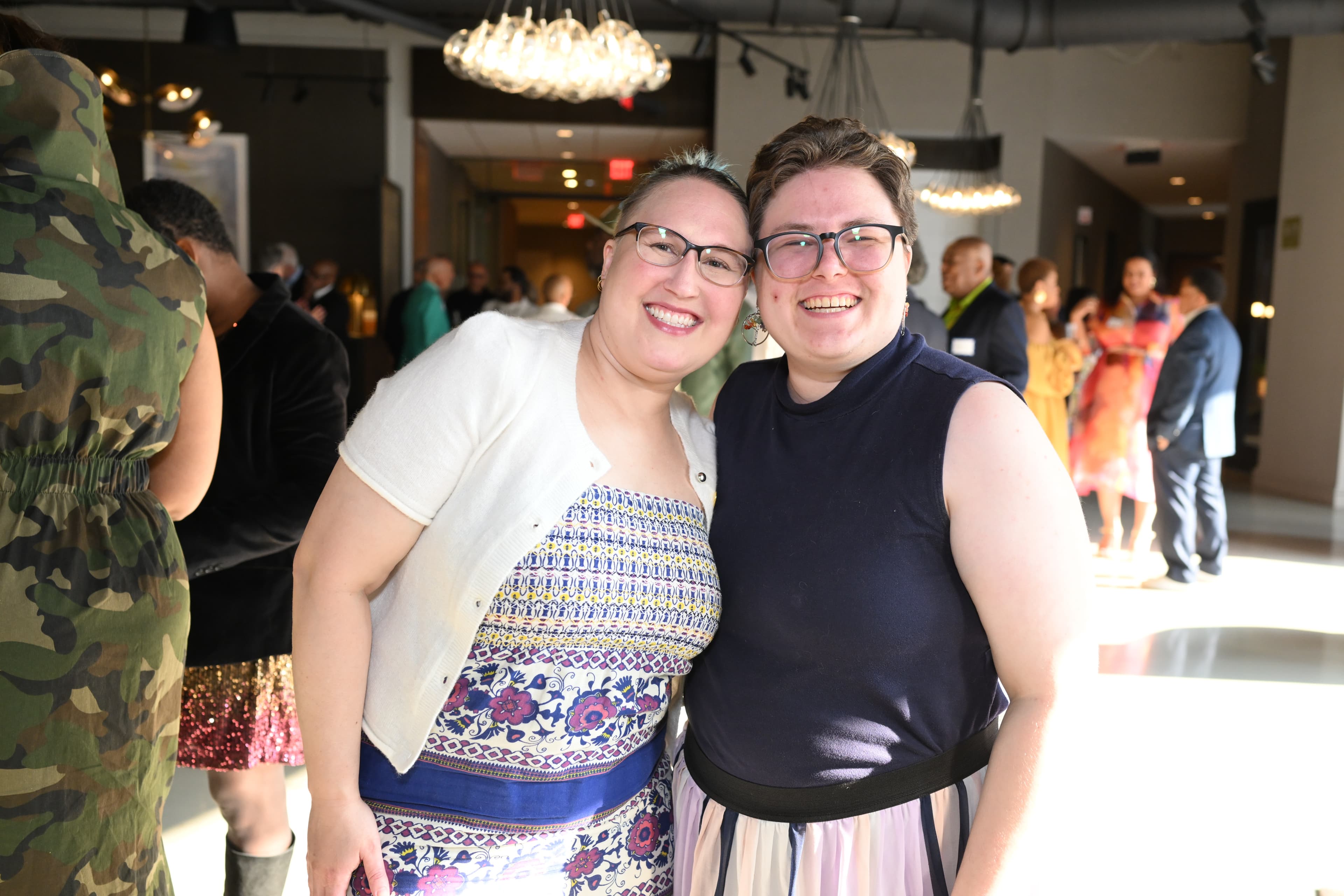 Two women with foreheads touching, smiling warmly, a crowd visible behind them.