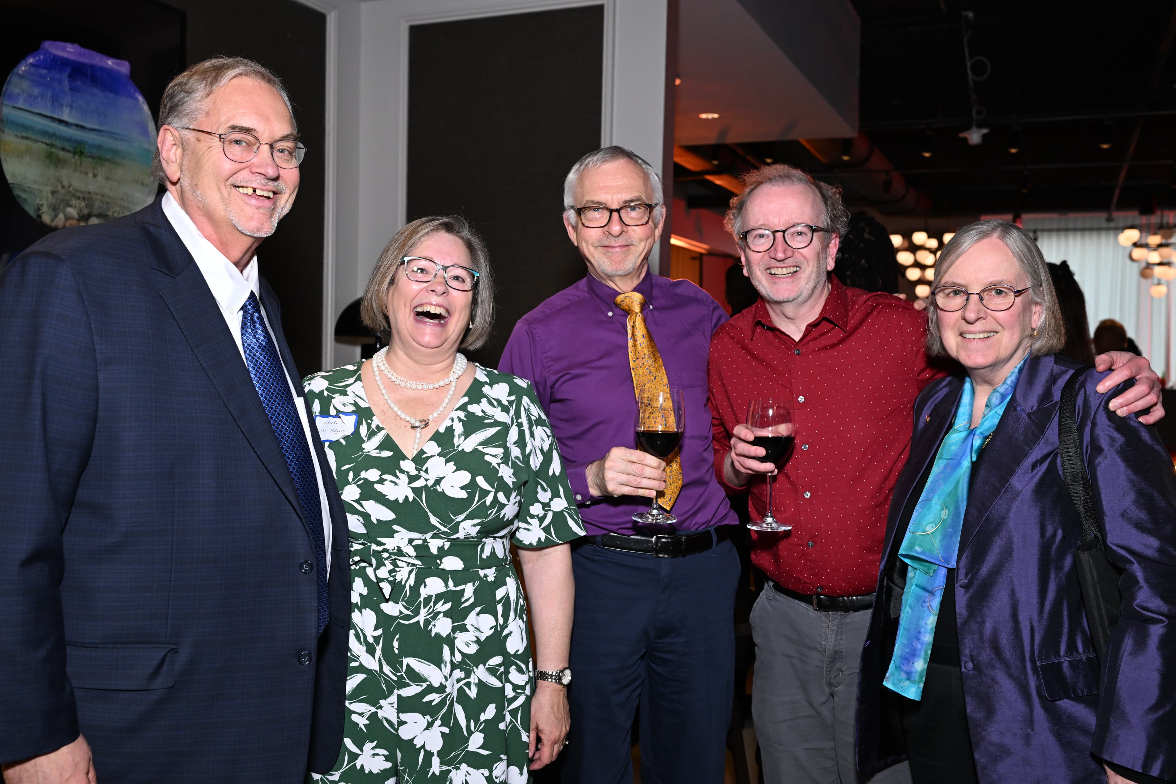 Five people gathered close, smiling, two holding wine glasses, in an elegant lounge.