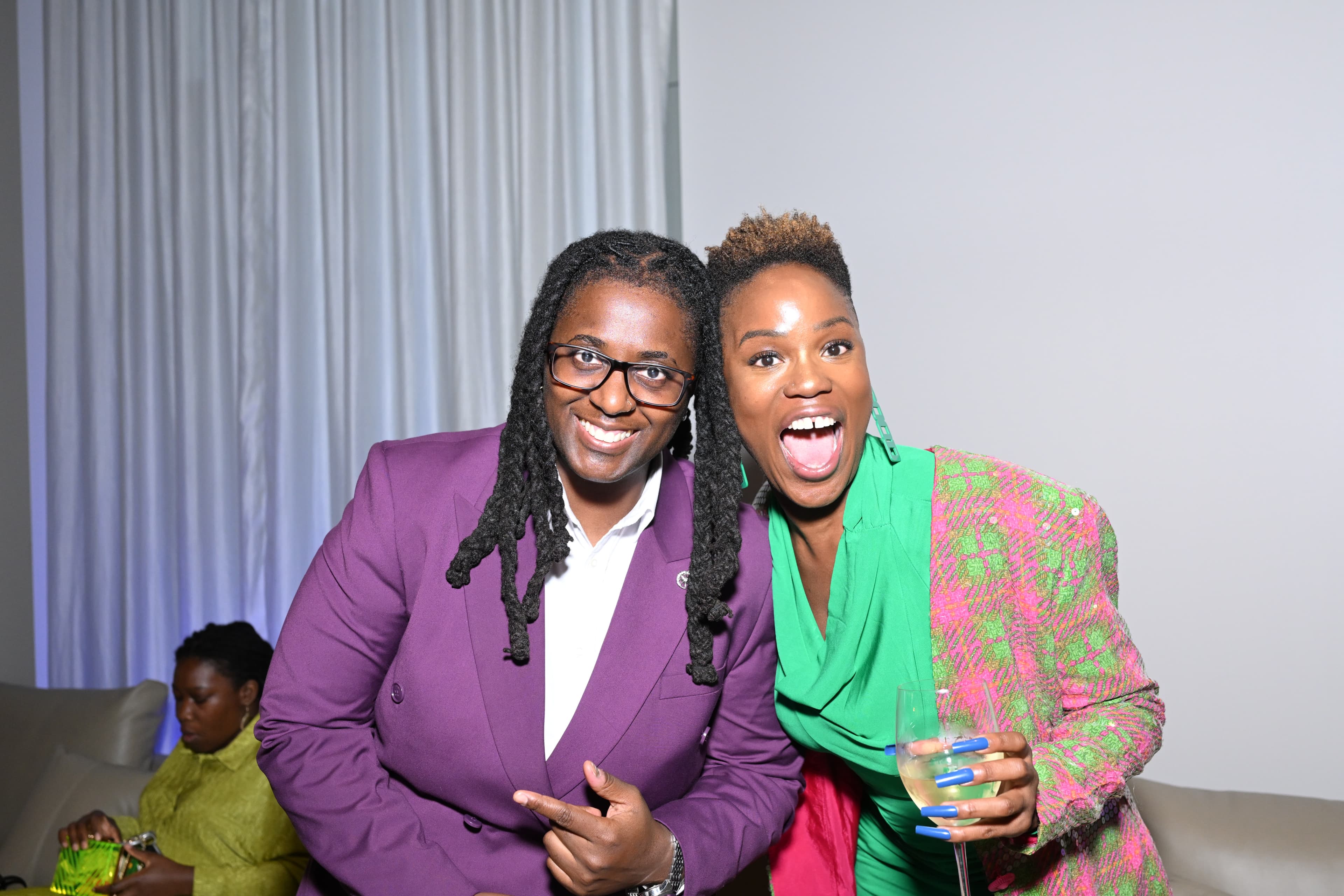 Two people laughing joyfully together, one in a purple suit, one in a green dress.
