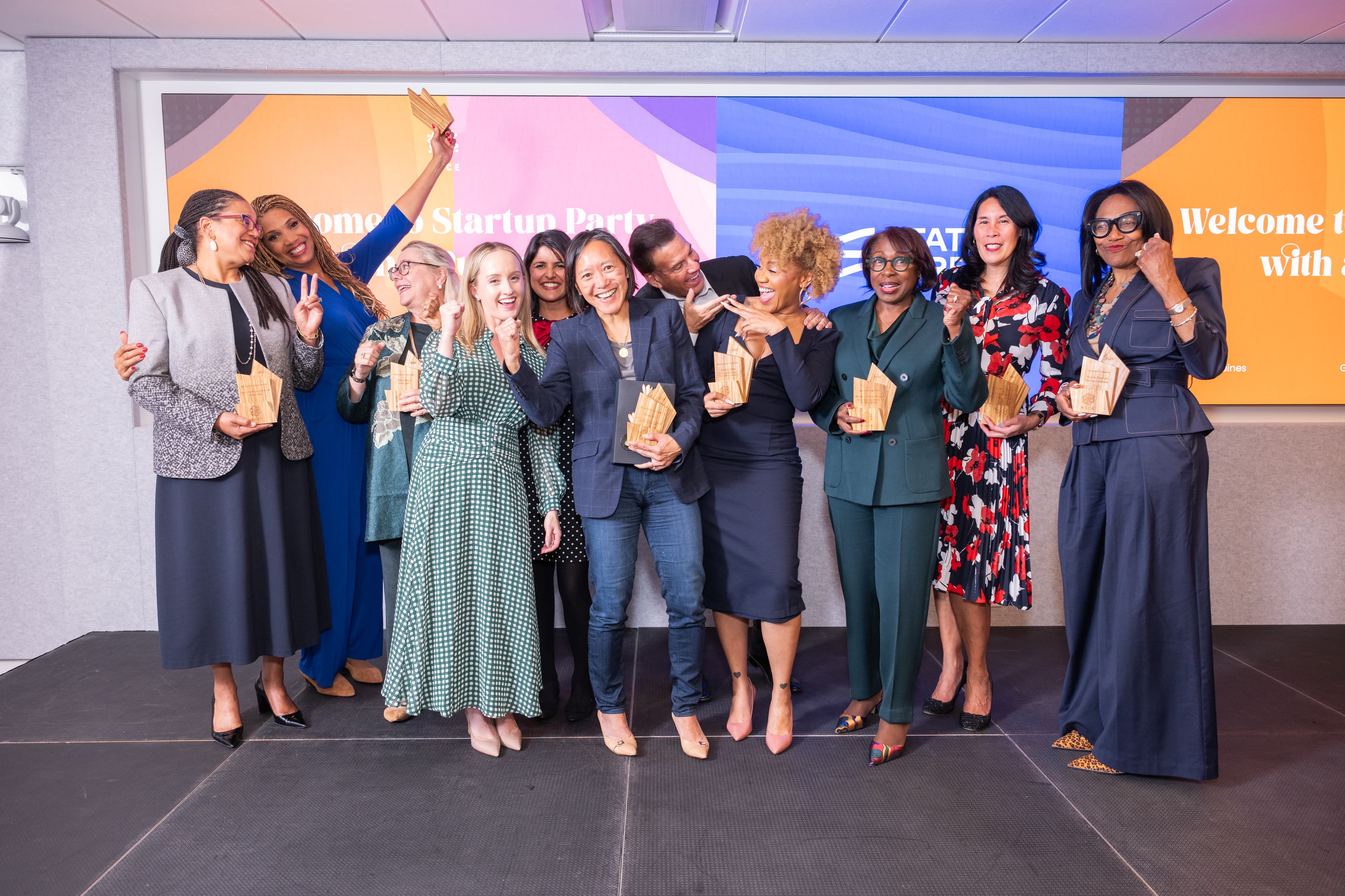 Ten people cheering together on a stage, holding wooden trophy-shaped awards.
