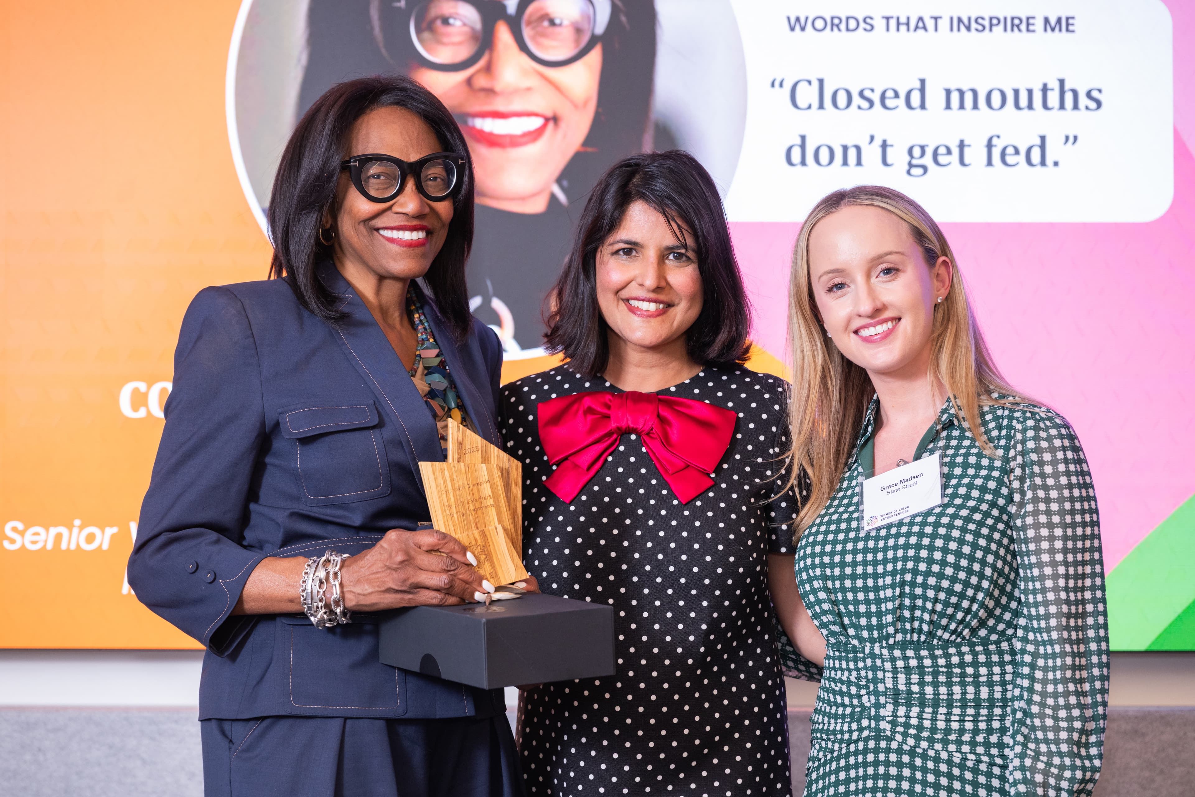Three women standing together, one holding a wooden award and a black box.