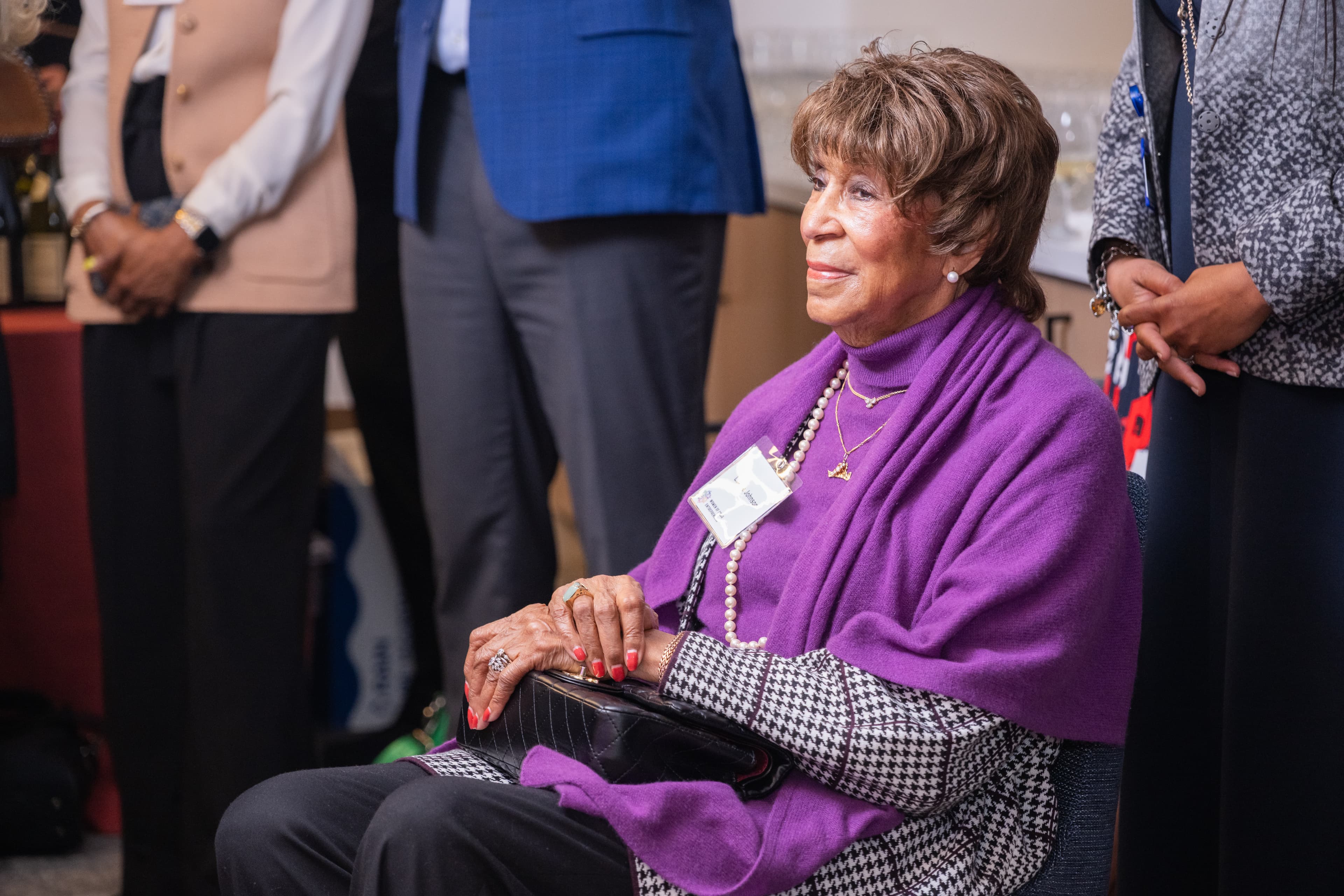Woman with a name badge sitting and smiling, two other people partially visible standing beside her.