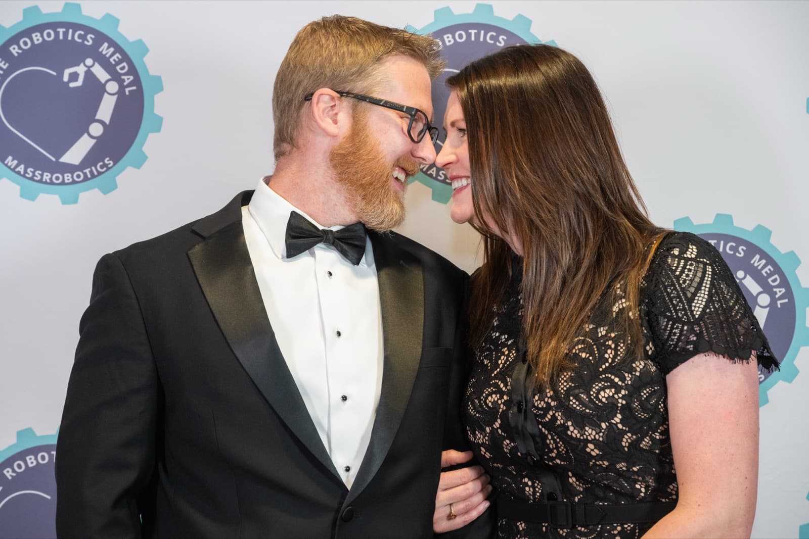 Two people with foreheads nearly touching, laughing, a bearded man in glasses and a woman with dark hair.