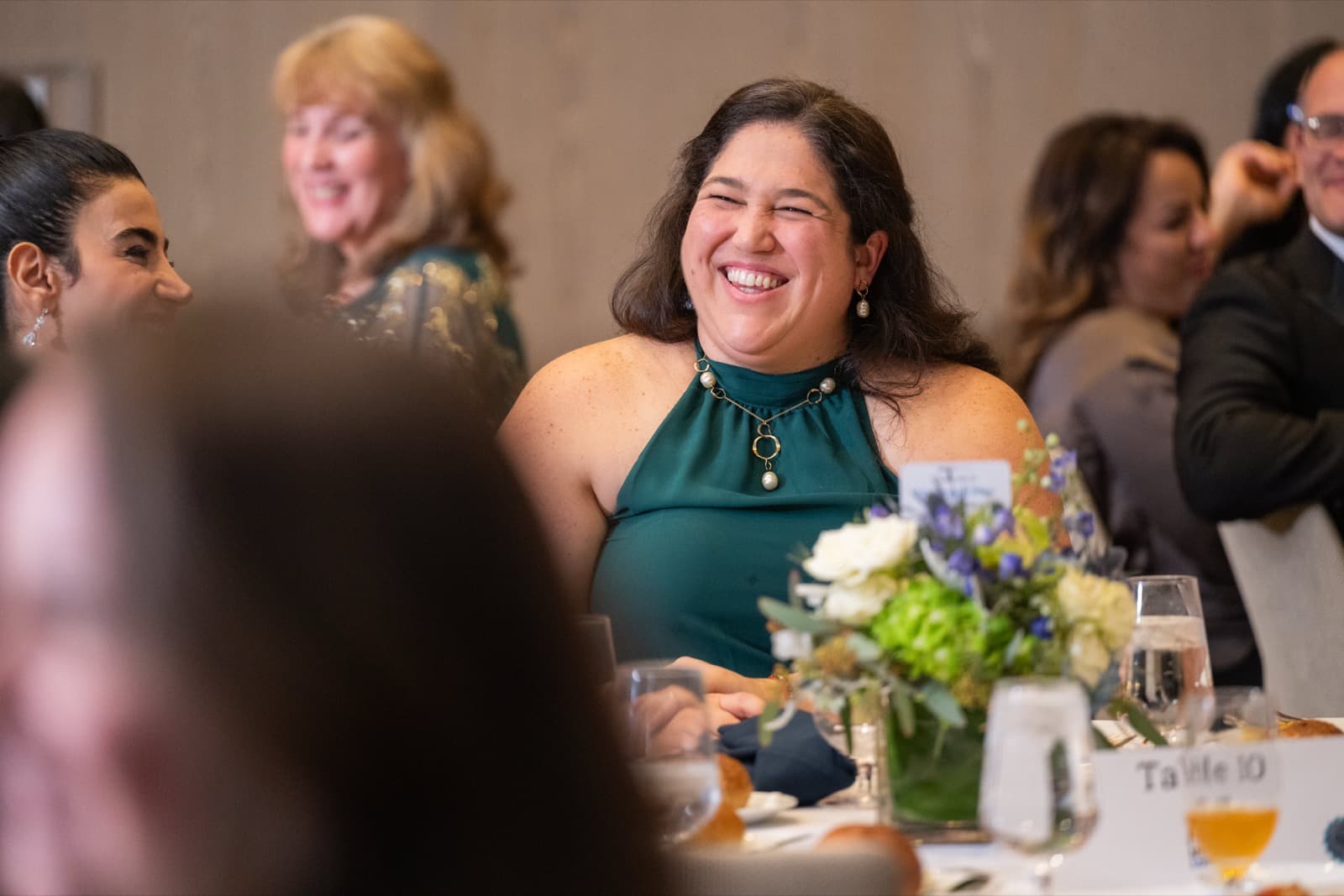 Woman laughing broadly at a gala dinner table, seated guests around her.