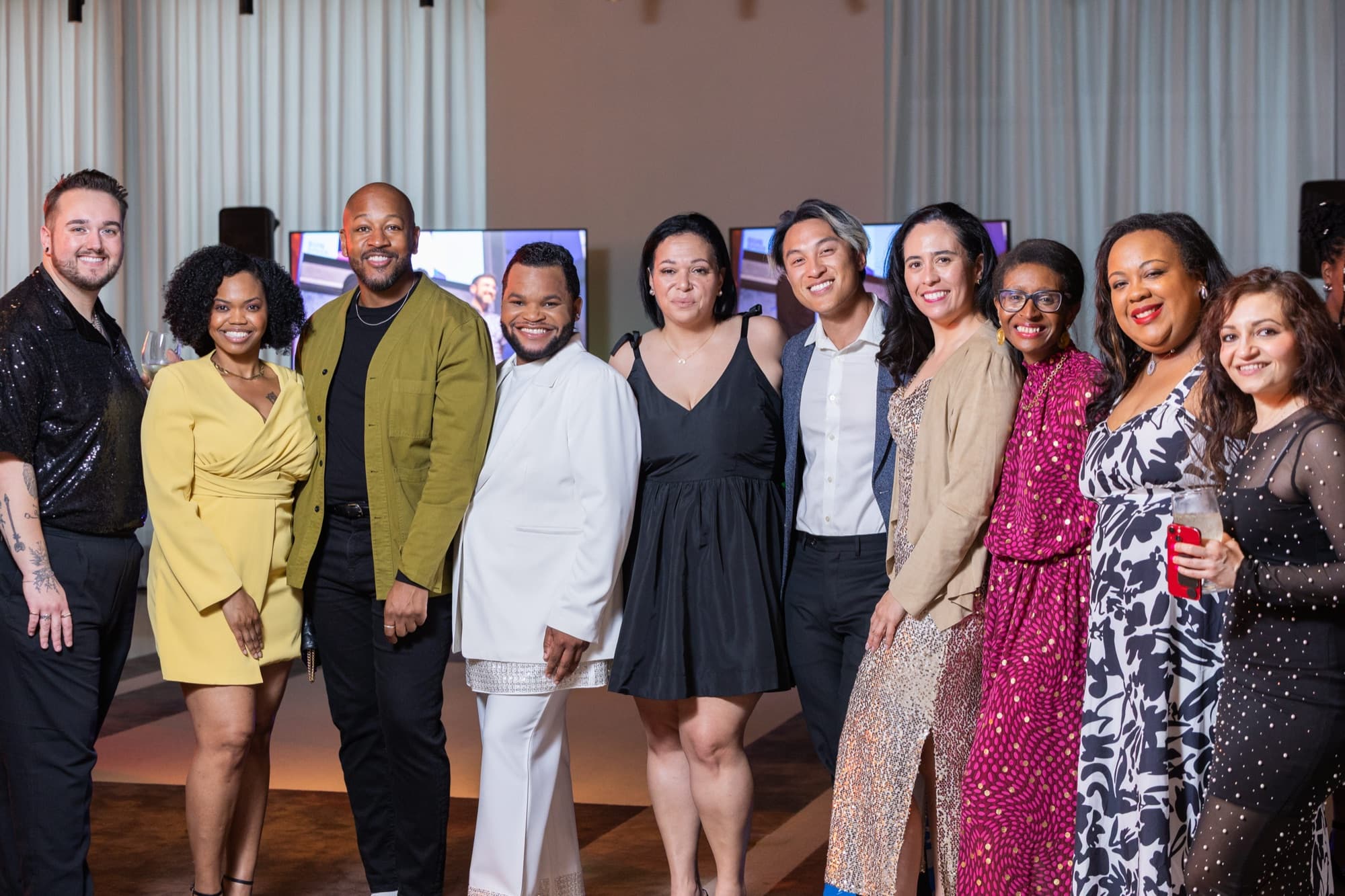 Ten people in colorful formal attire posing together for a group photo indoors, smiling.